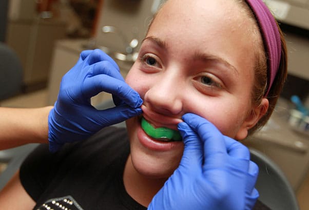 Girl getting fitted with a green mouthguard by a person wearing blue gloves.